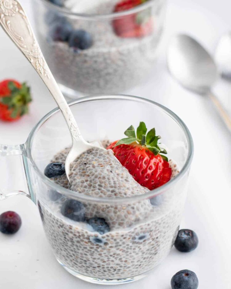 a cup with chia pudding and topped with strawberry and blueberries, plus a spoon in it