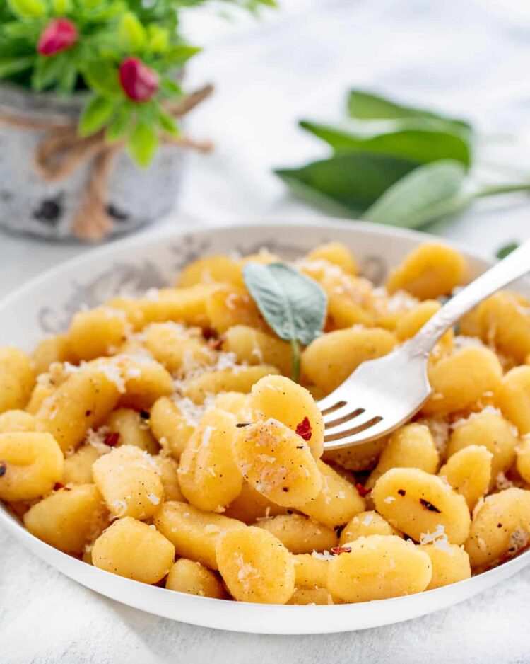 gnocchi in a white plate garnished with parmesan cheese and sage