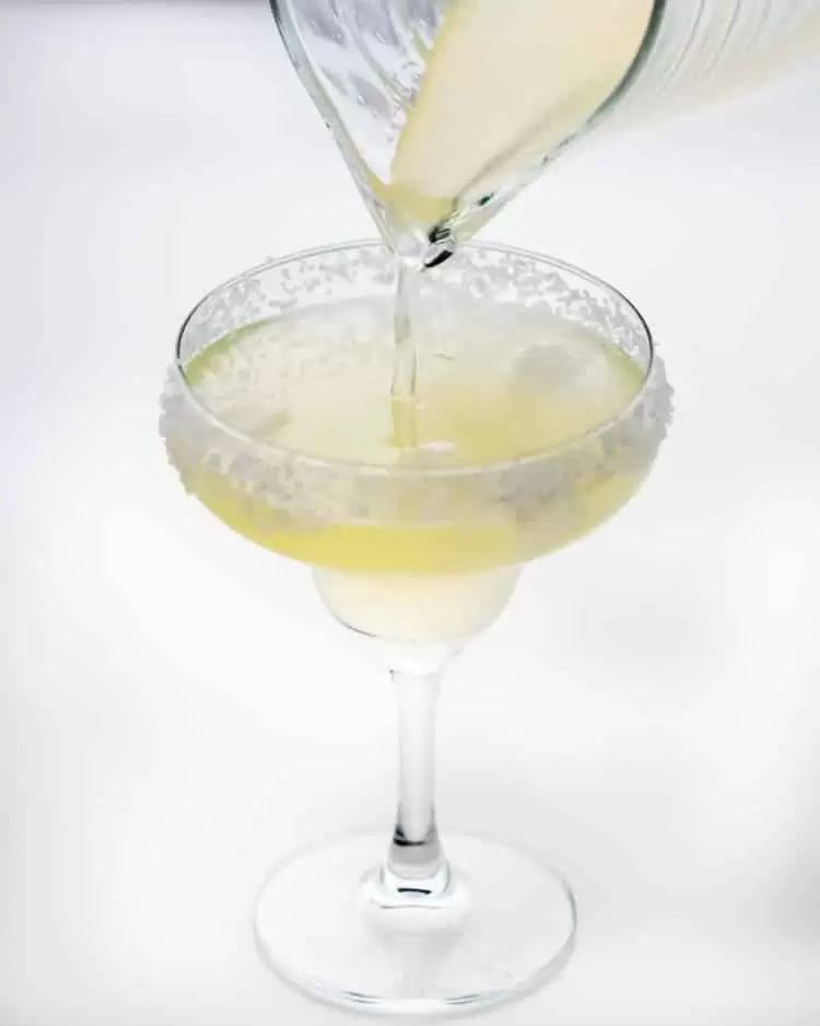 pouring margarita in a rimmed glass