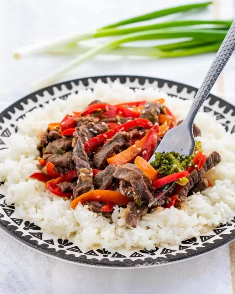beef stir fry over rice in a plate with a fork in it