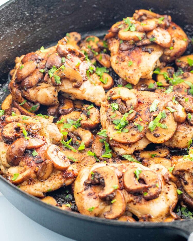 skillet chicken and mushrooms in a black skillet garnished with parsley