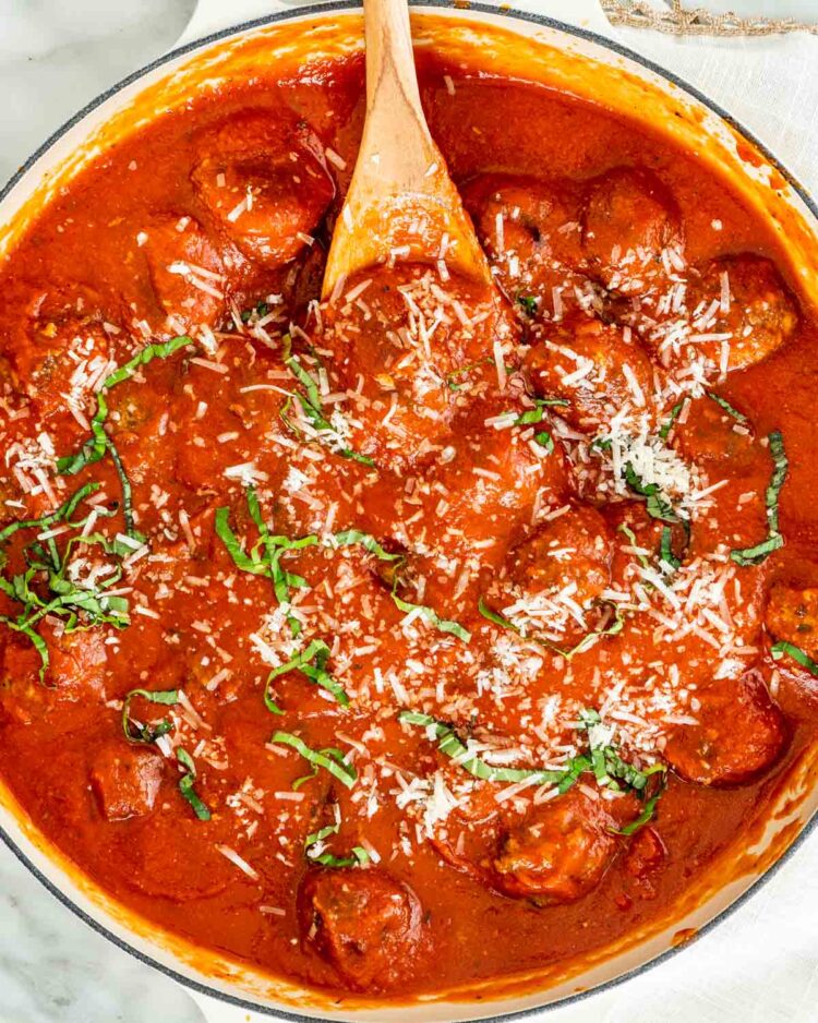 overhead shot of a large skillet with marinara sauce and meatballs garnished with parmesan cheese and basil