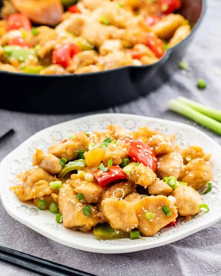 sweet and sour chicken on a white plate with a skillet in the background