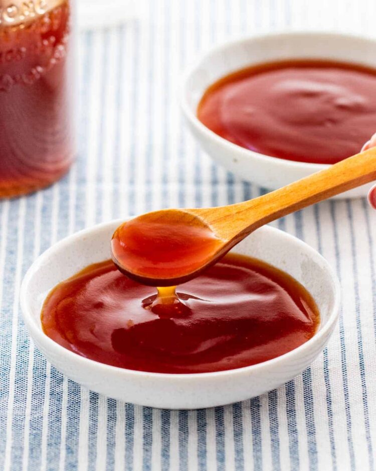 sweet and sour sauce in a small white dish with a wooden spoon in it