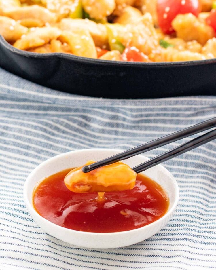 chop sticks dipping a piece of chicken in sweet and sour sauce