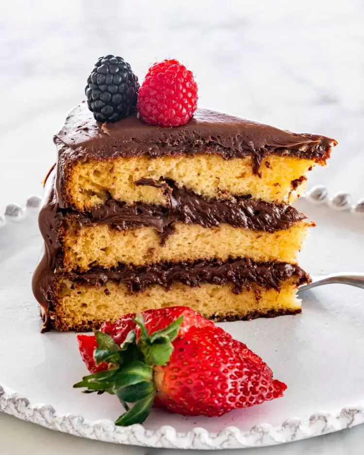 a slice of yellow cake with chocolate frosting and berries