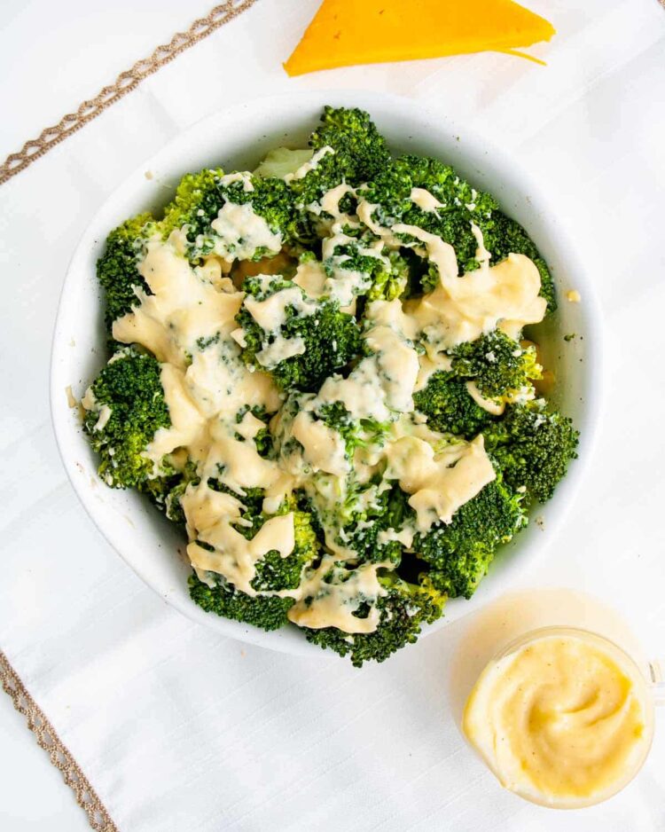 overhead shot of a bowl full of steamed broccoli with cheese sauce