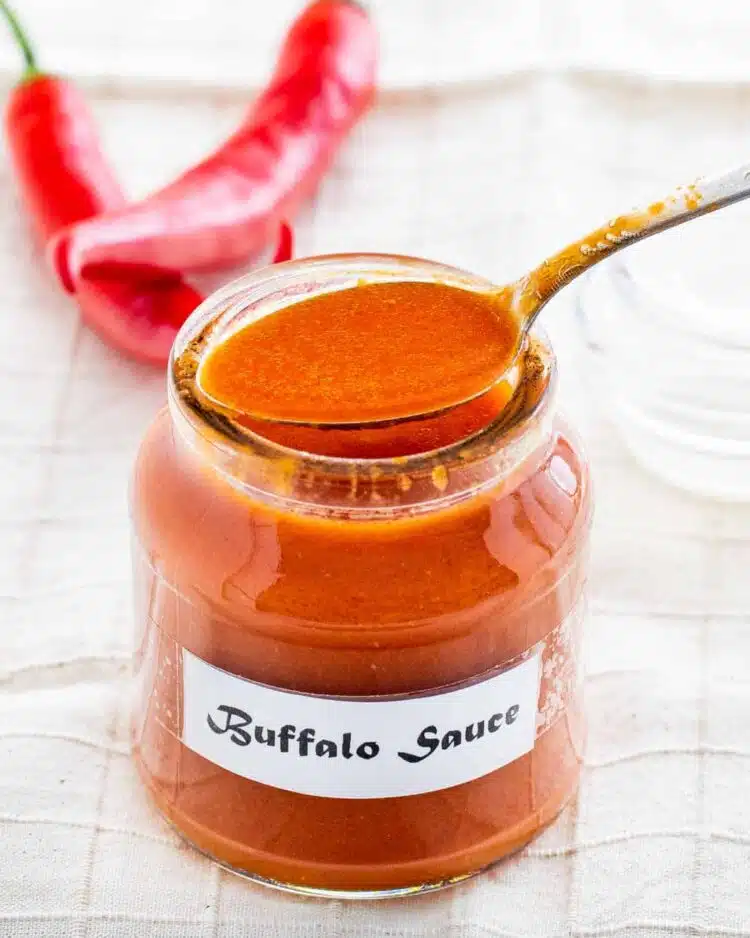 a spoon filled with buffalo sauce sitting atop a jar