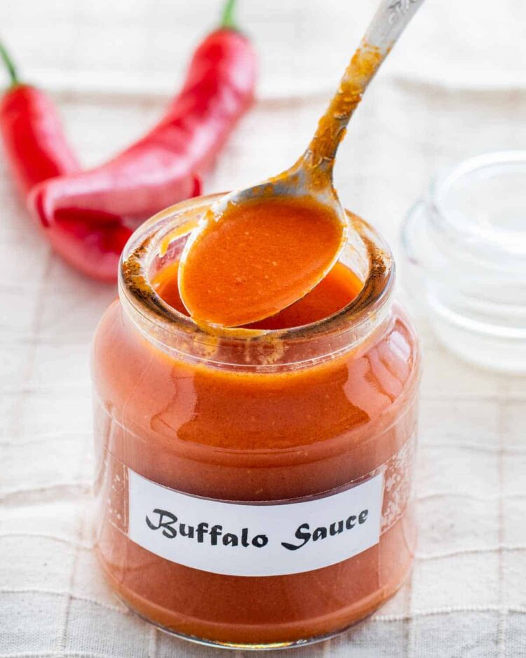 a jar with homemade buffalo sauce and a tablespoon sitting on top