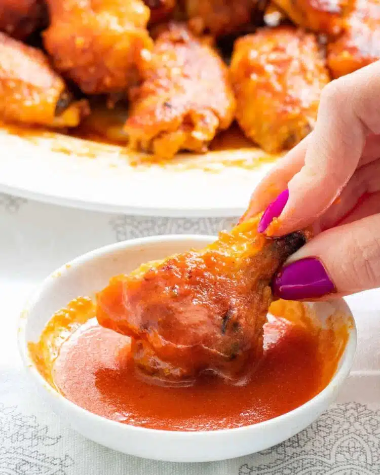 a hand dipping a wing in buffalo sauce