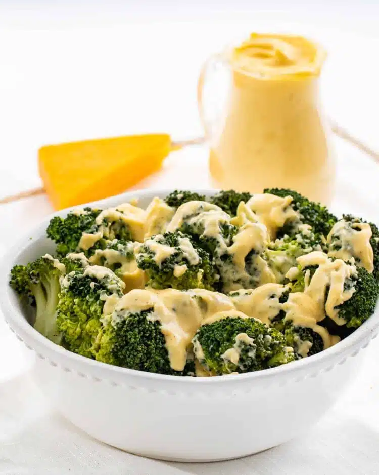 steamed broccoli in a white bowl drizzled with cheese sauce
