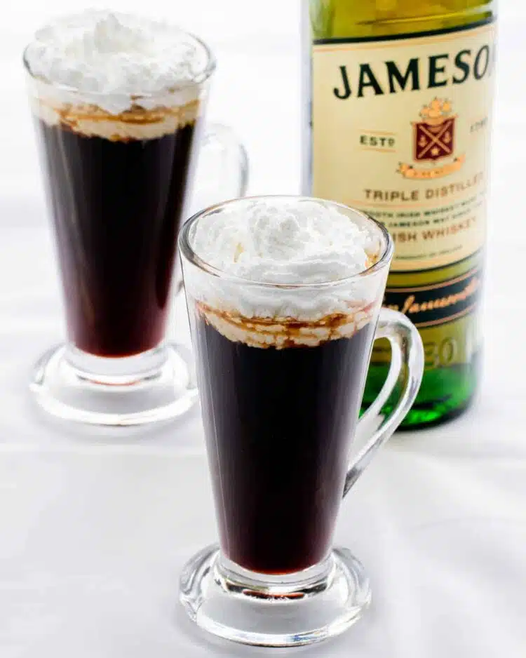 two glass cups with irish coffee and a bottle of whiskey in the background