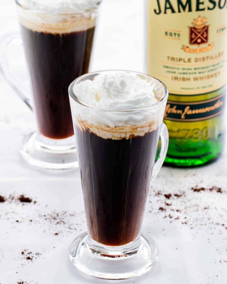 two glass cups with irish coffee and a bottle of whiskey in the background