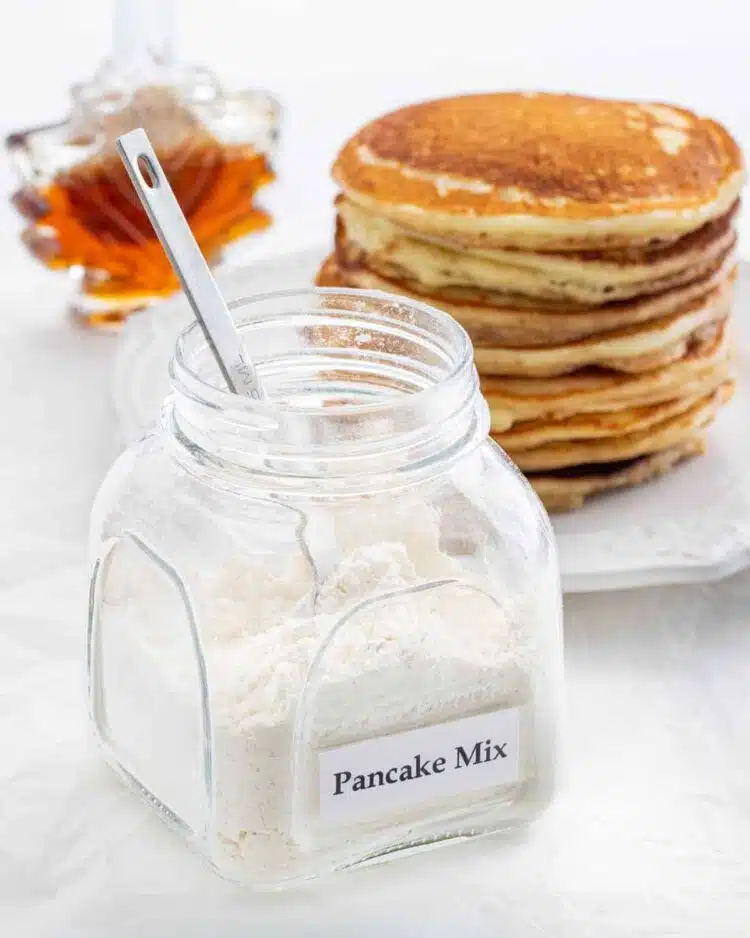 a jar with pancake mix and a stack of pancakes in the background