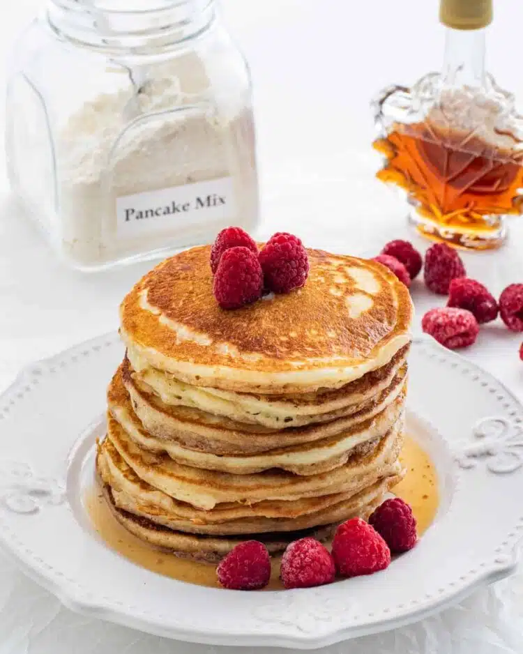 a stack of pancakes on a white plate garnished with raspberries