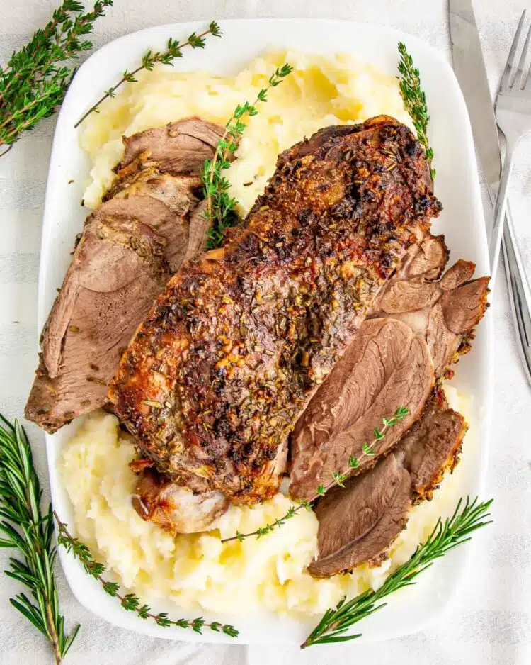 overhead shot of roast leg of lamb over mashed potatoes on a serving platter
