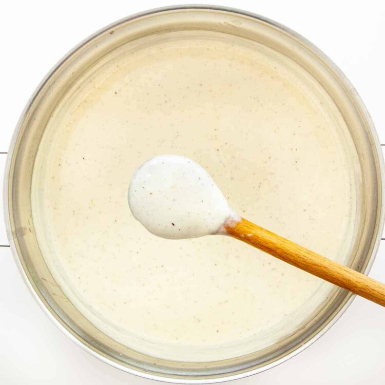 overhead shot of alfredo sauce in a saucepan with a wooden spoon over it