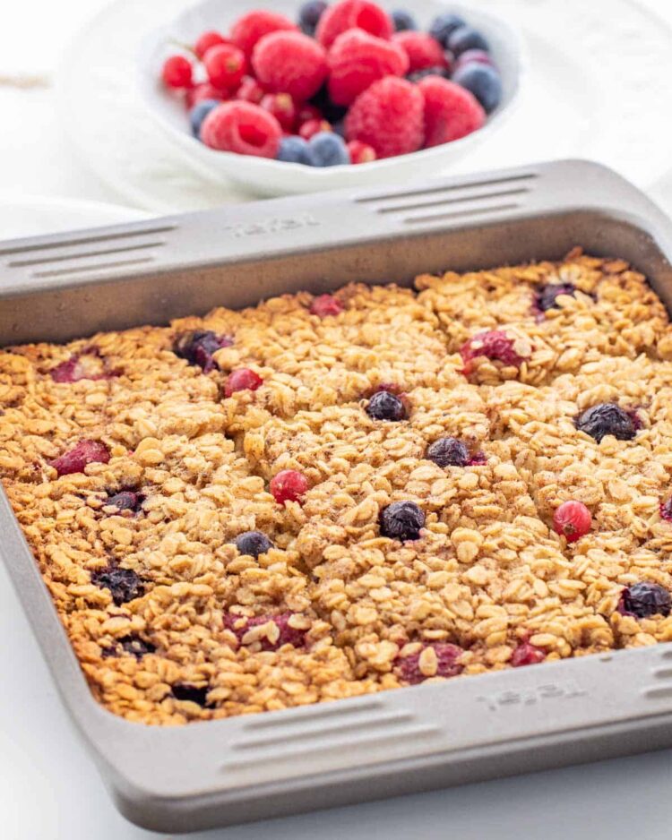 a pan with baked oatmeal and a bowl of berries in the background