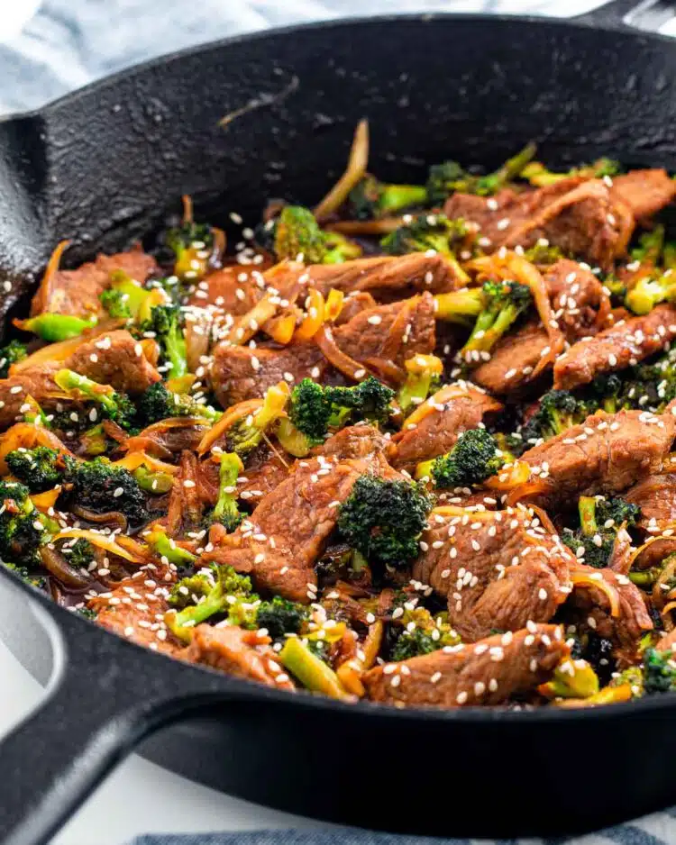 beef and broccoli in a black skillet garnished with sesame seeds