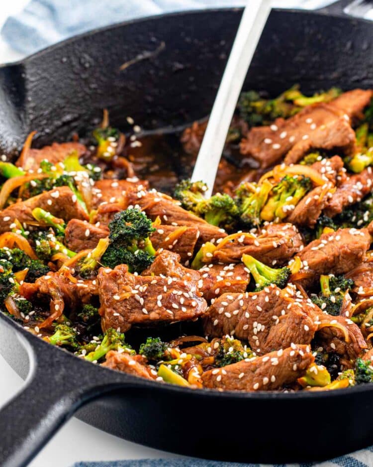 beef and broccoli in a black skillet with a serving spoon inside
