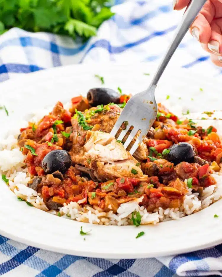 side shot of chicken cacciatore over a bed of rice with a fork holding a piece of chicken