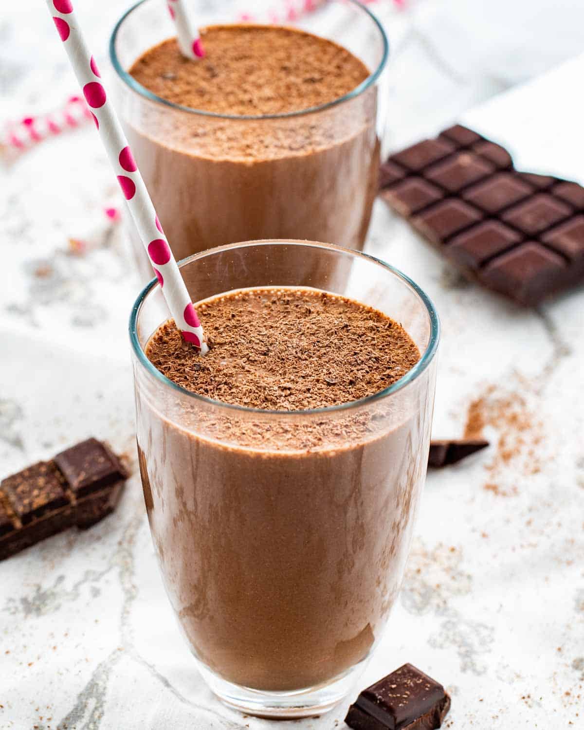 two glasses filled with chocolate smoothies each with a straw inside