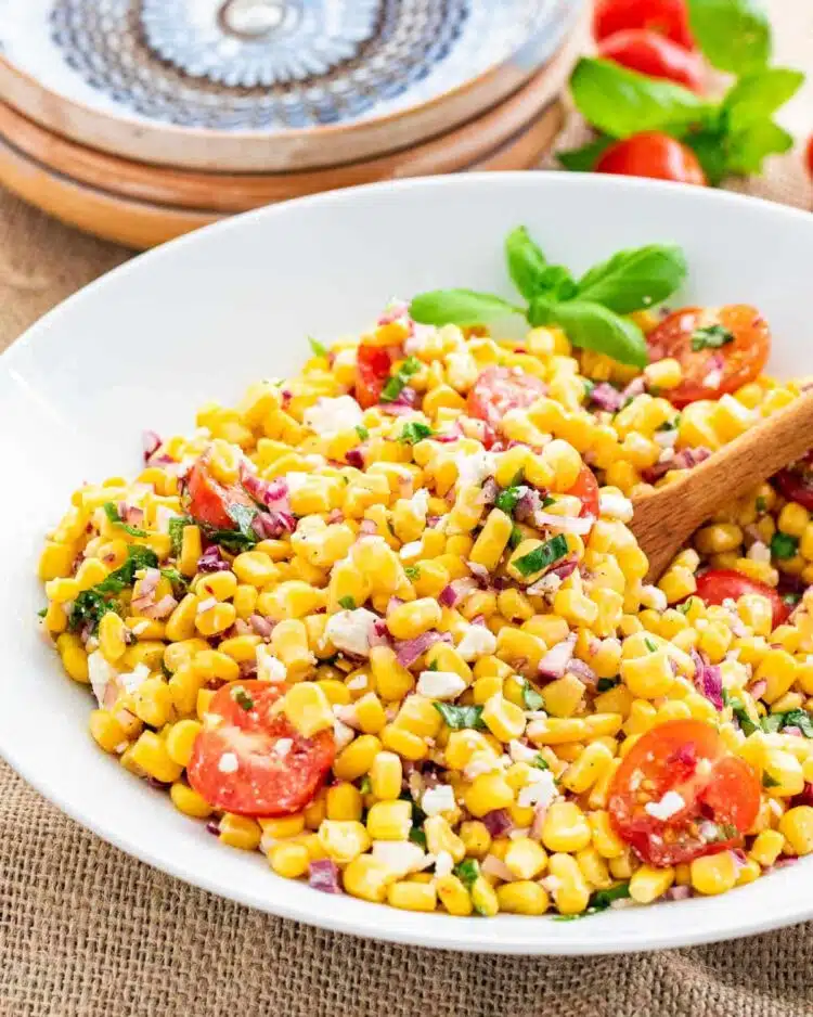 side shot of delicious and vibrant corn salad in a white bowl with a wooden spoon inside