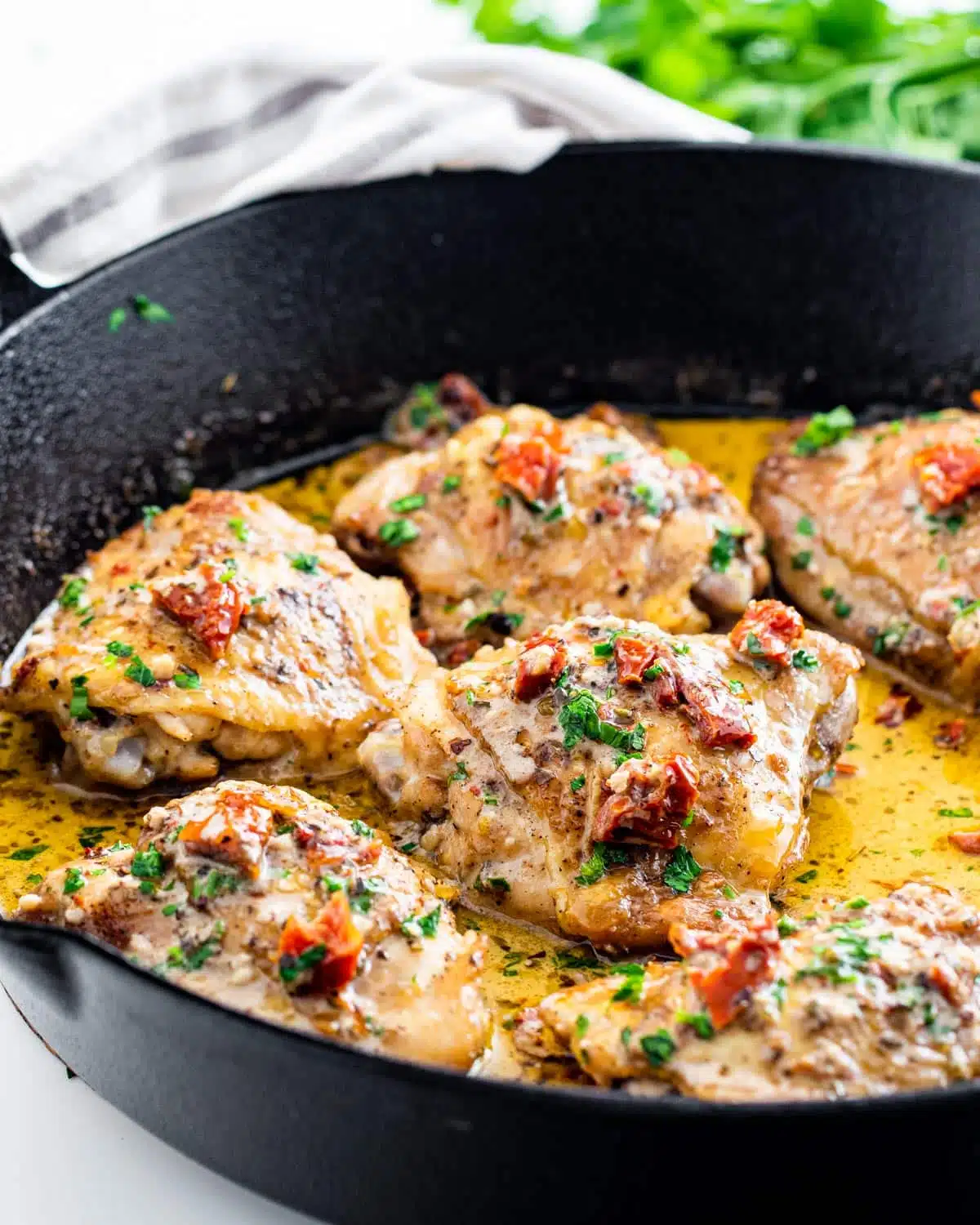 side shot of chicken thighs in a black skillet with a creamy sun-dried tomato sauce