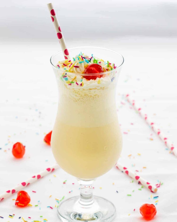 a vanilla milkshake in a glass topped with maraschino cherries and sprinkles