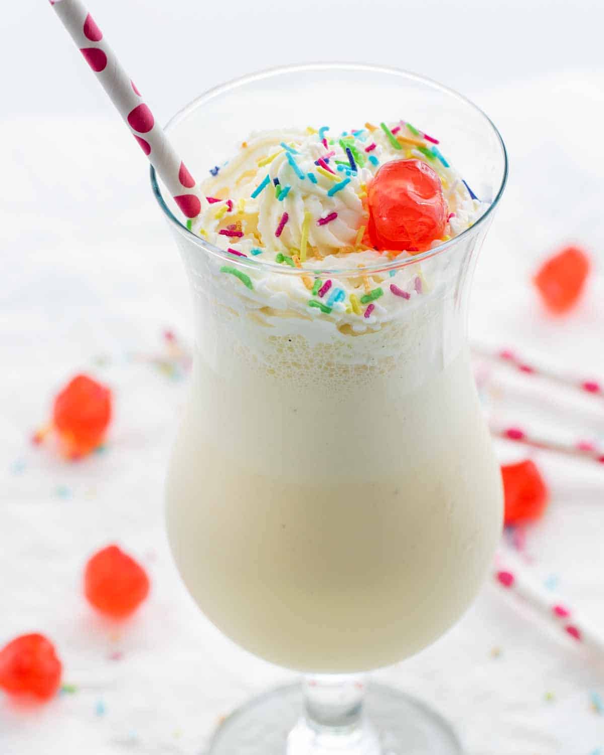 a milkshake in a glass topped with maraschino cherry and sprinkles
