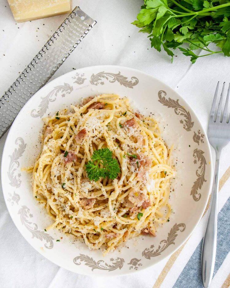 overhead shot of spaghetti carbonara in a plate garnished with parsley and parmesan cheese