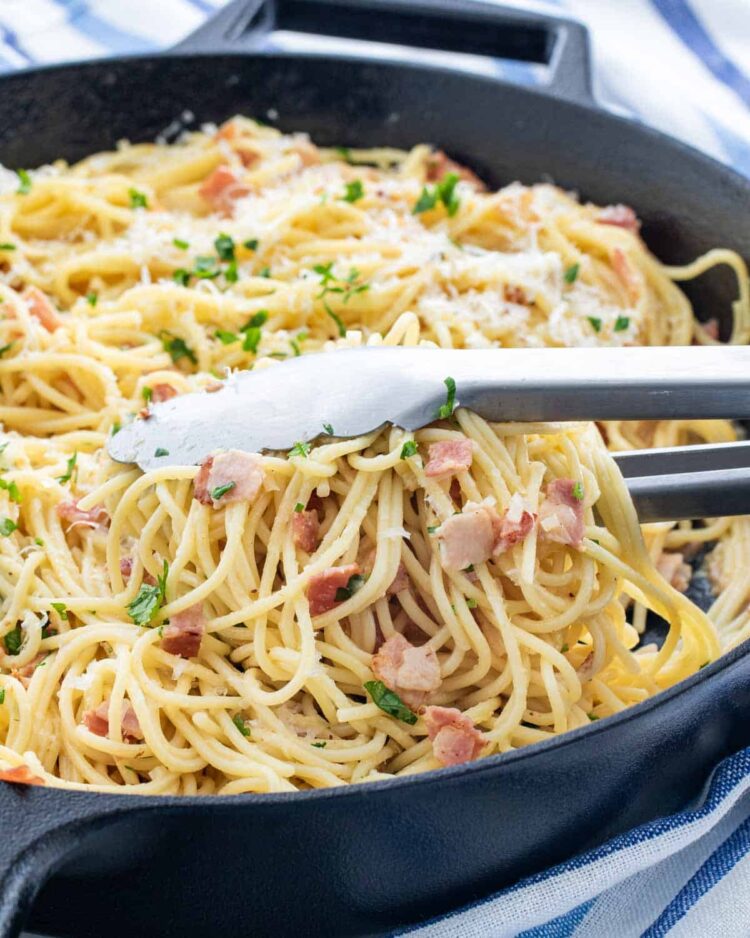 spaghetti carbonara with a pair of tongs in a black skillet