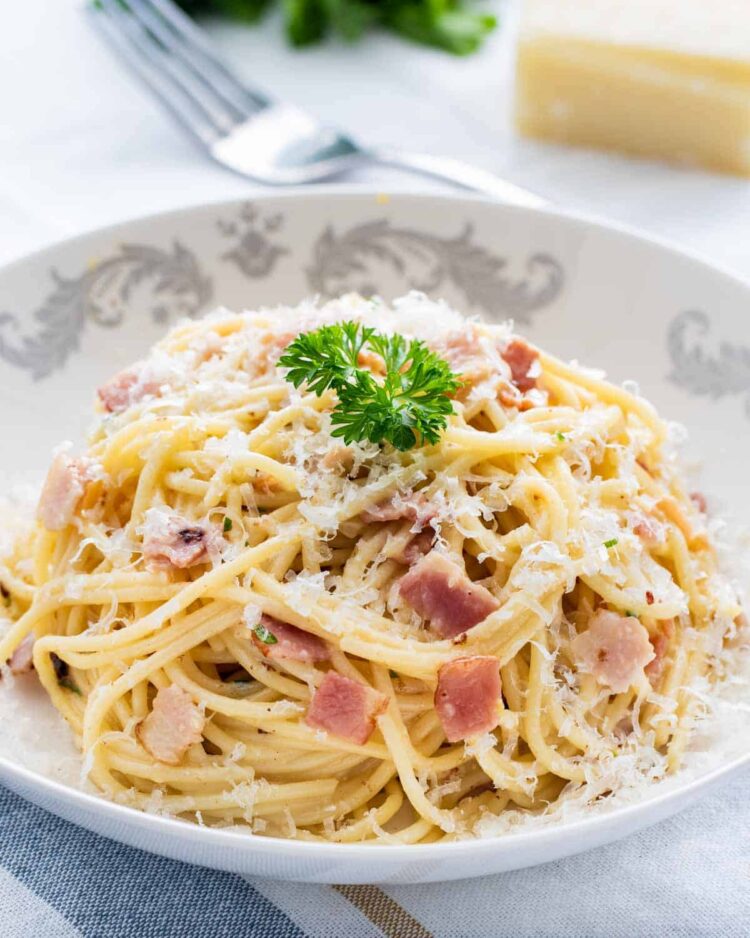 a place full of spaghetti carbonara garnished with parsley and parmesan cheese