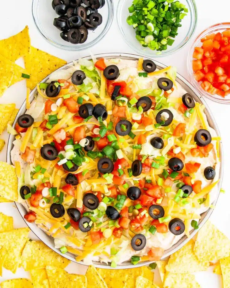 overhead shot of taco dip on a platter topped with cheese, olives, tomatoes and green onions