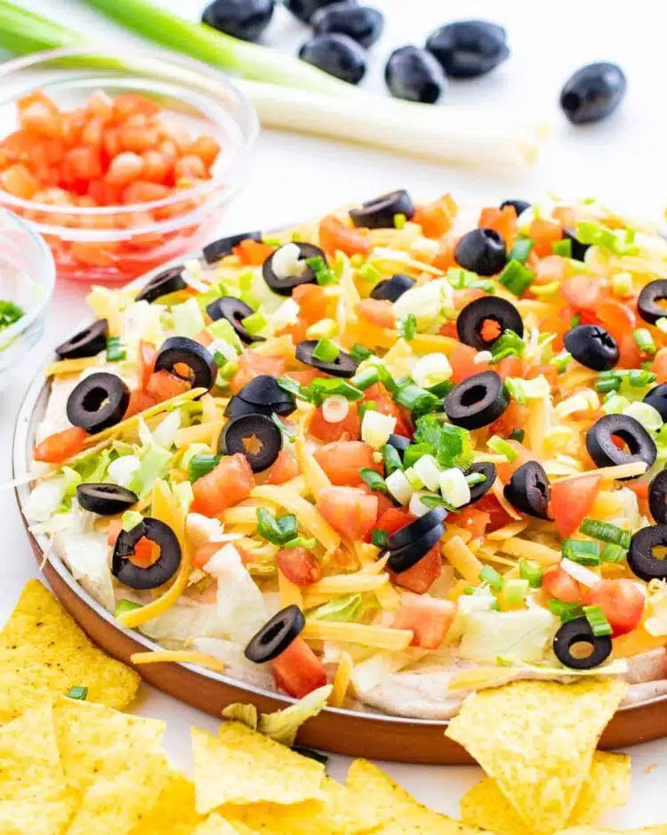 taco dip on a platter topped with cheese, olives, tomatoes and green onions