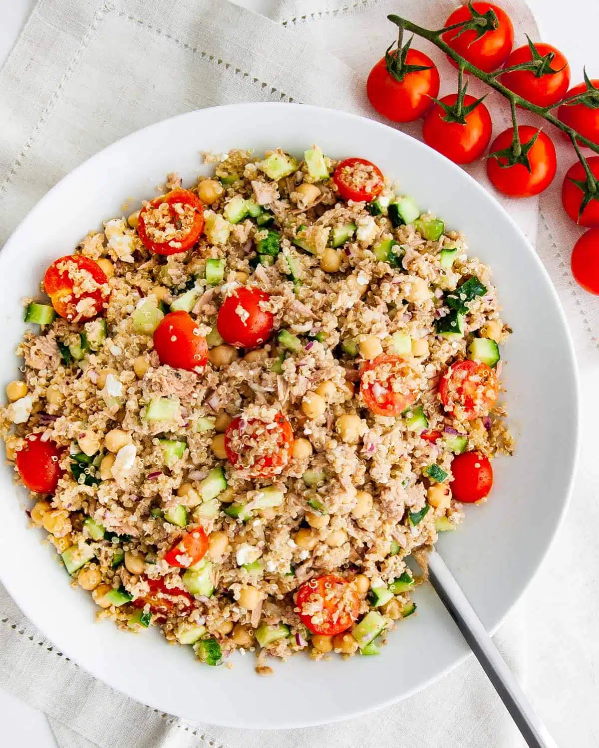 overhead shot of tuna quinoa salad with tomatoes and cucumbers in a white bowl