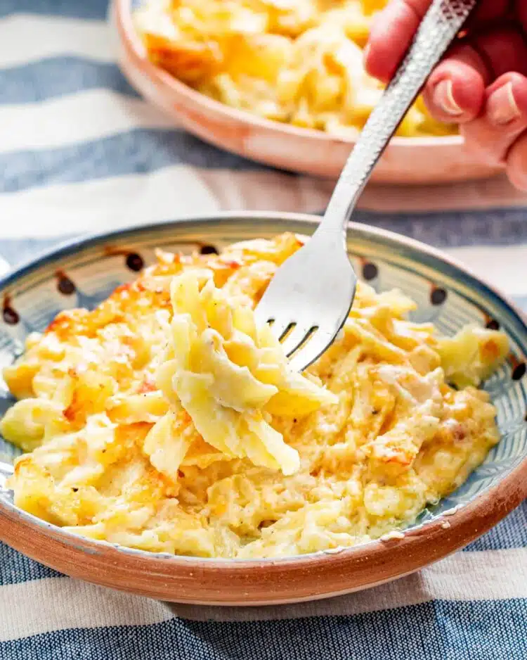 a fork picking up some cheesy potato casserole from a plateful of it