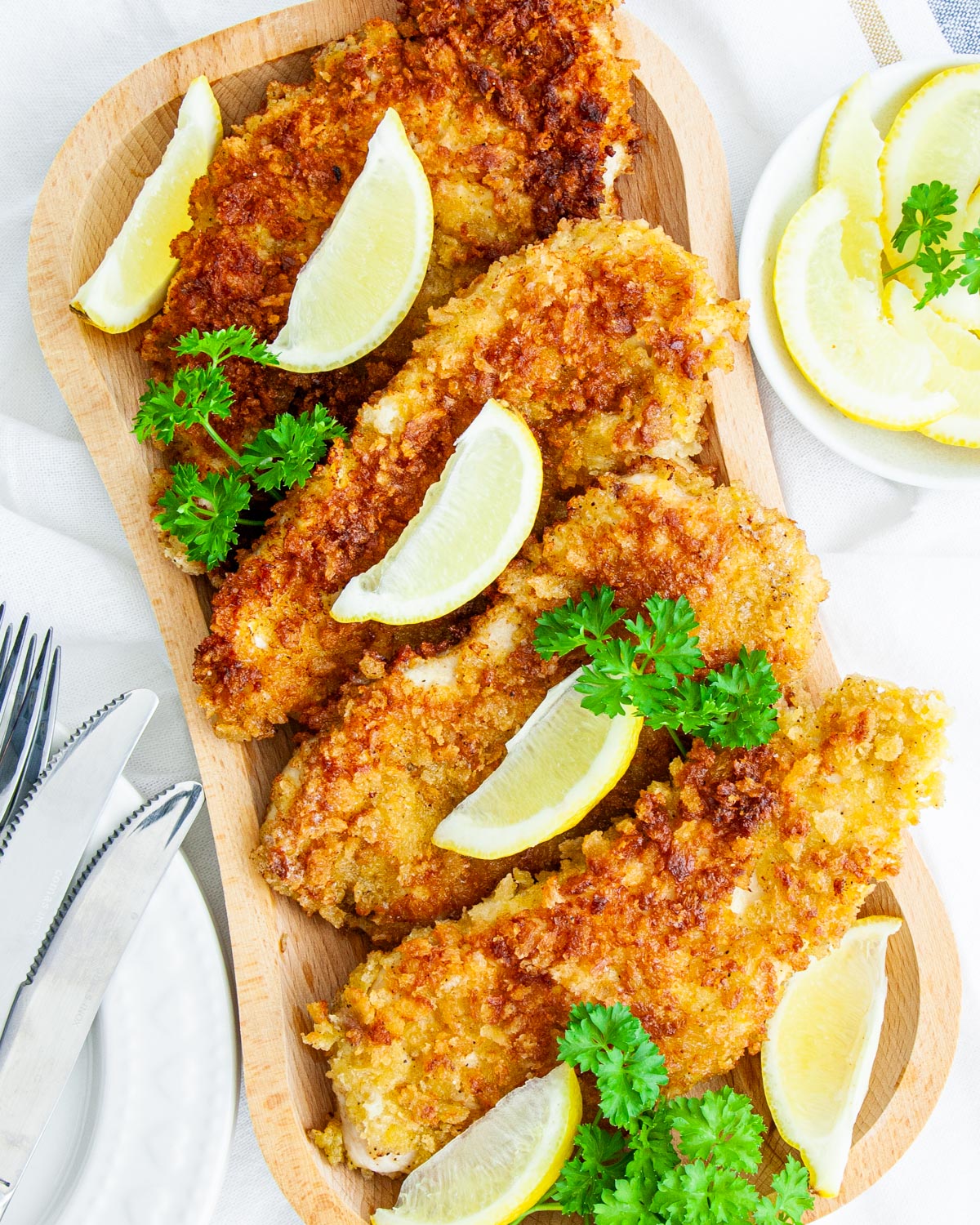 overhead shot of chicken cutlets on a wooden platter garnished with lemon wedges and parsley