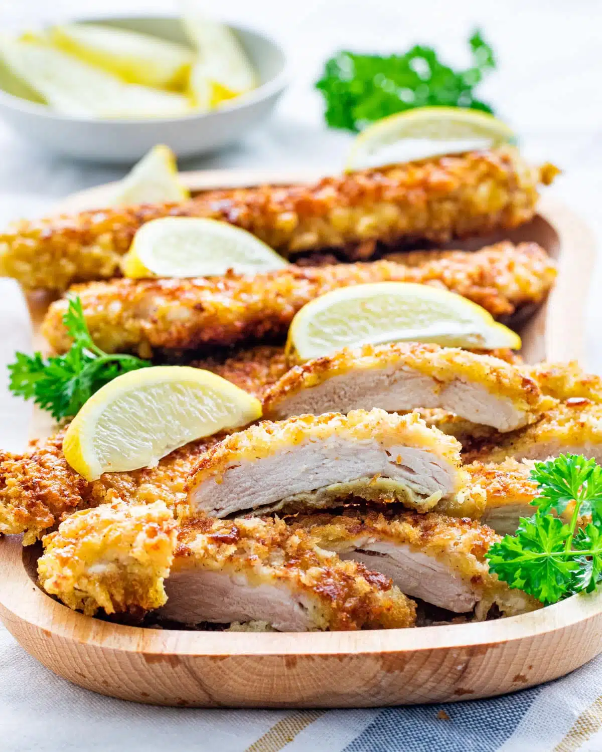 crispy chicken cutlets cut into pieces on a wooden plate garnished with lemon wedges and parsley