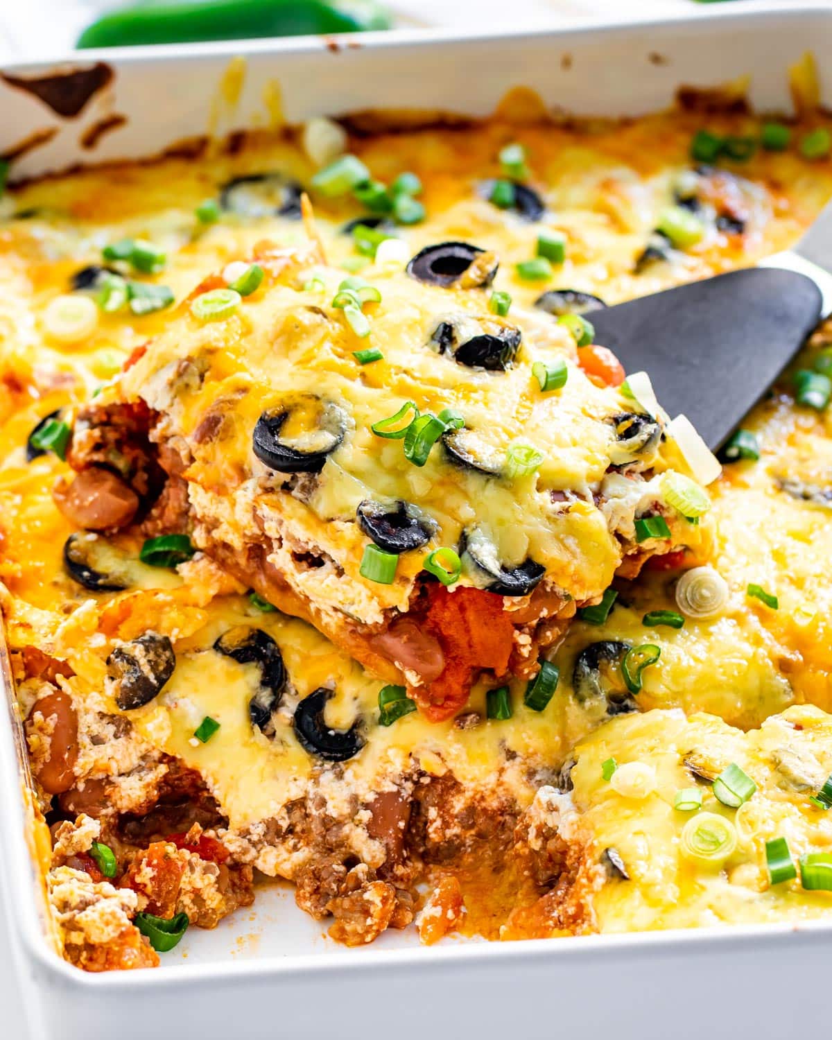 mexican casserole in a casserole dish fresh out of the oven with a cut slice on a spatula laying on top