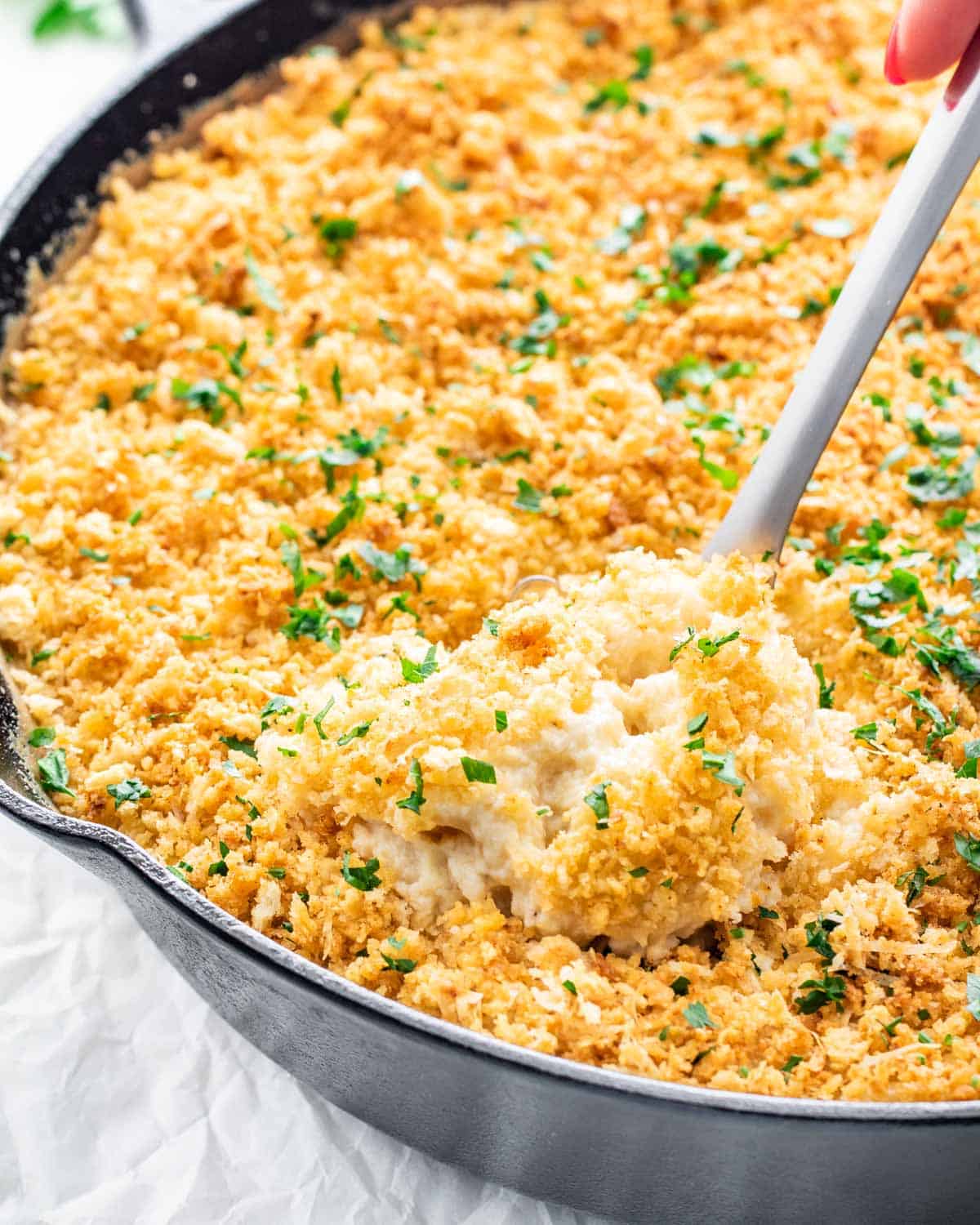 baked mac and cheese fresh out of the oven with a serving spoon inside and garnished with parsley