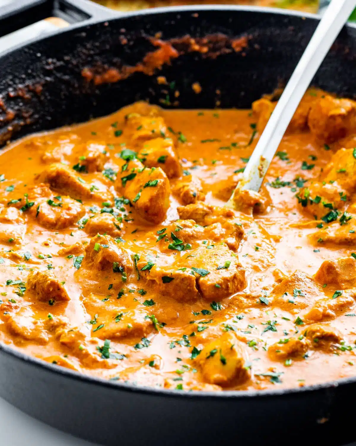 side view shot of freshly made butter chicken garnished with parsley in a black skillet