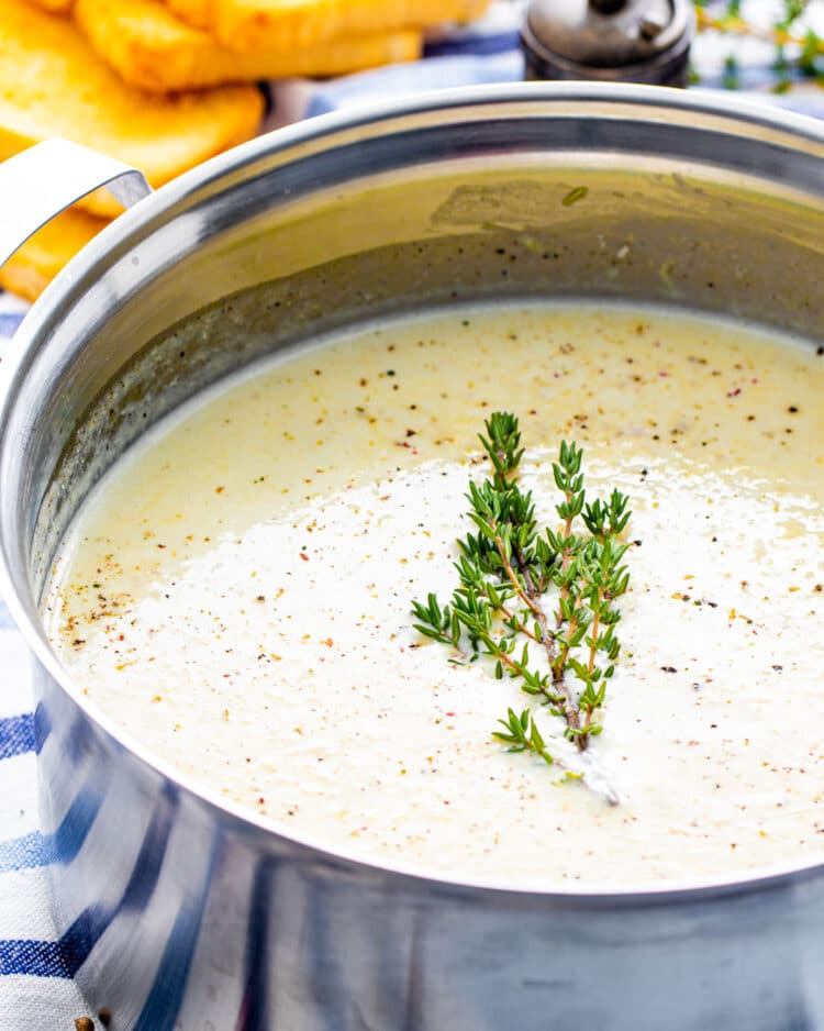 side view shot of cream of cauliflower in a soup pot garnished with fresh thyme and pepper