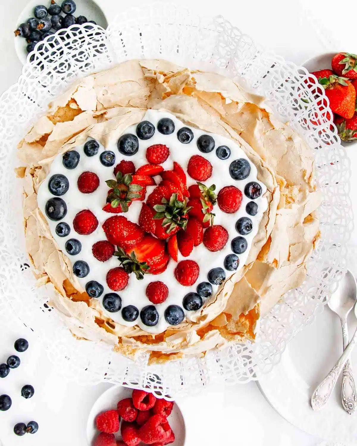 overhead shot of a gorgeous pavlova on a cake platter topped with whipped cream and berries