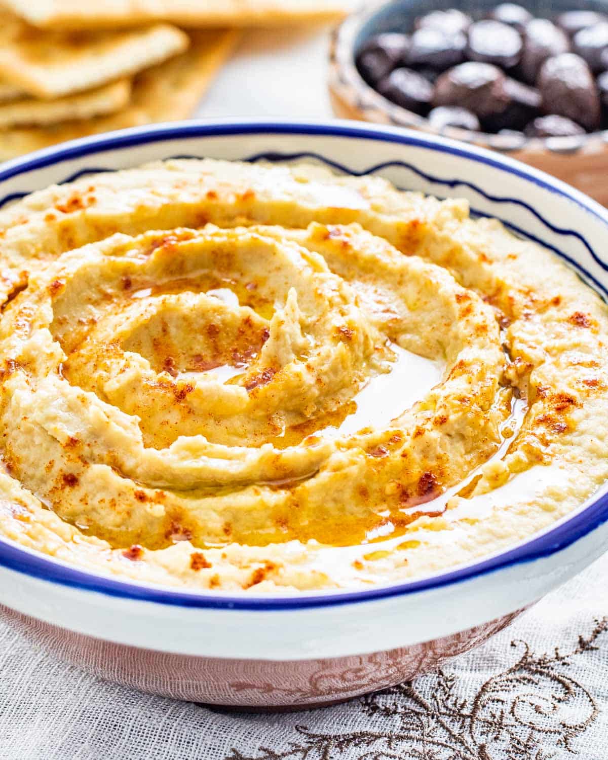 sideview shot of a bowl filled with freshly made hummus drizzled with olive oil and sprinkled with a bit of paprika