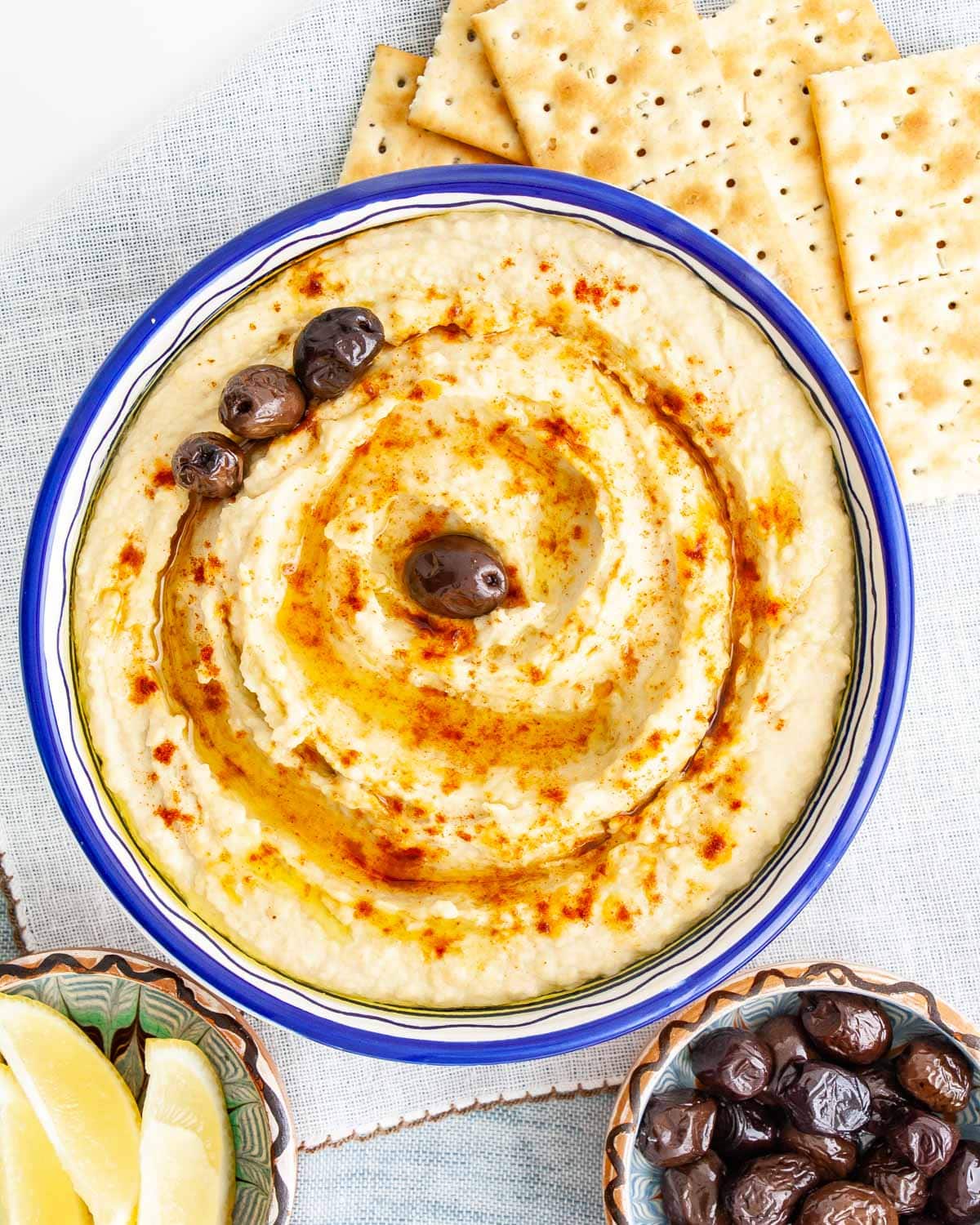 overhead shot of a bowl filled with freshly made hummus drizzled with olive oil and sprinkled with a bit of paprika and a few olives