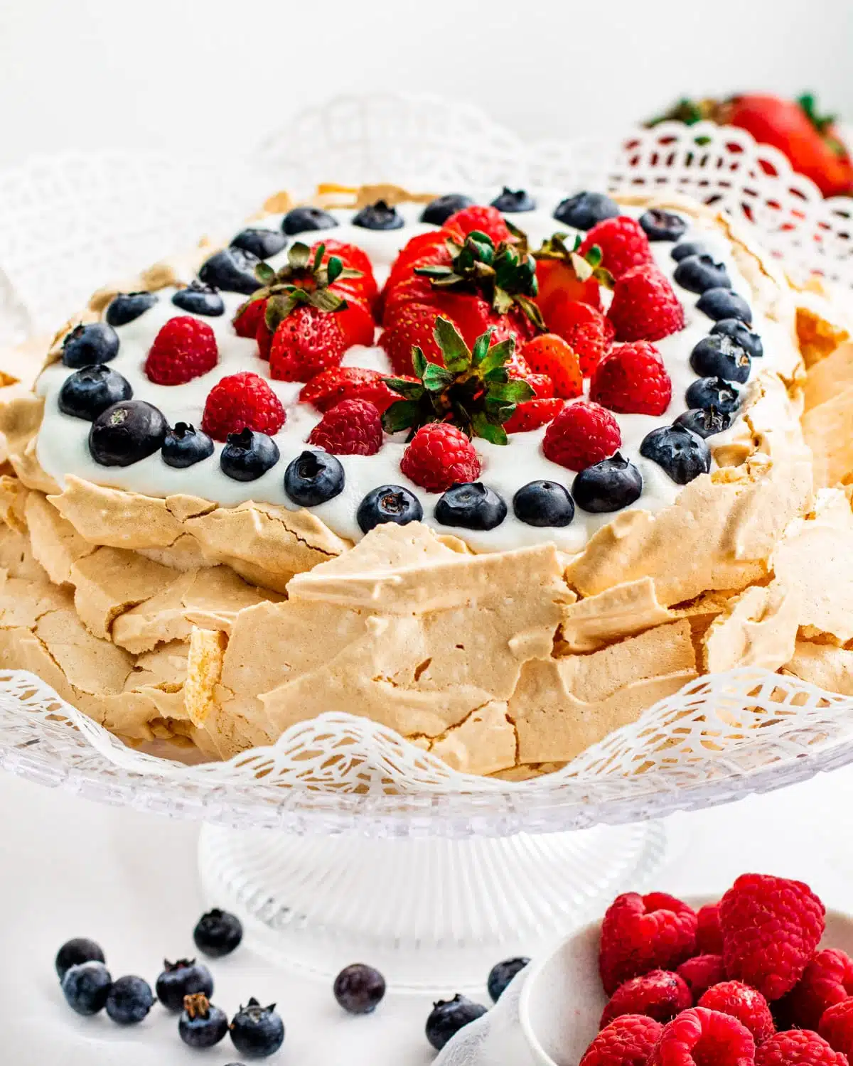 a gorgeous pavlova on a cake plate topped with whipped cream and berries