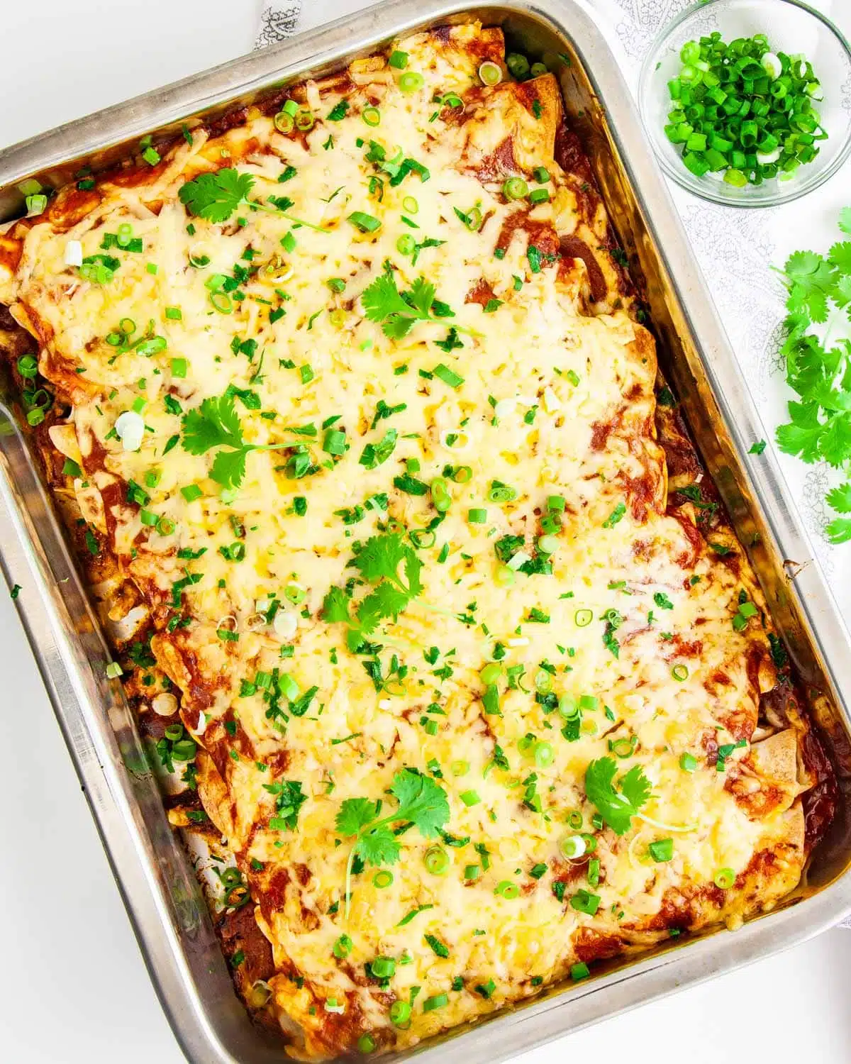 overhead shot of chicken enchiladas in a casserole dish garnished with cilantro and green onions
