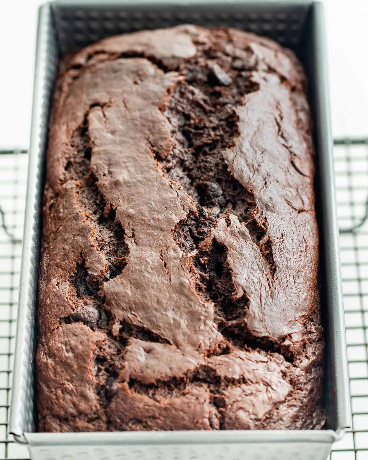 side view shot of a chocolate chip banana bread in a loaf tin on a cooling rack fresh out of the oven