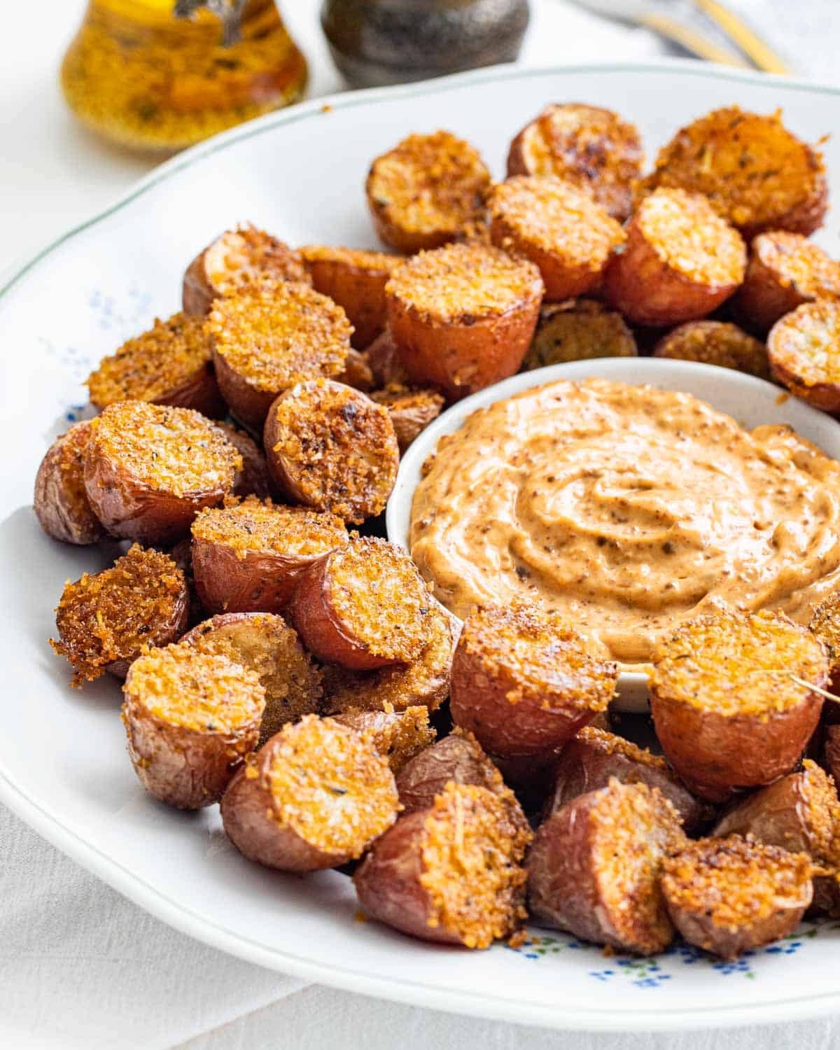crispy parmesan potatoes on a white plate with a bowl in the middle with dipping sauce
